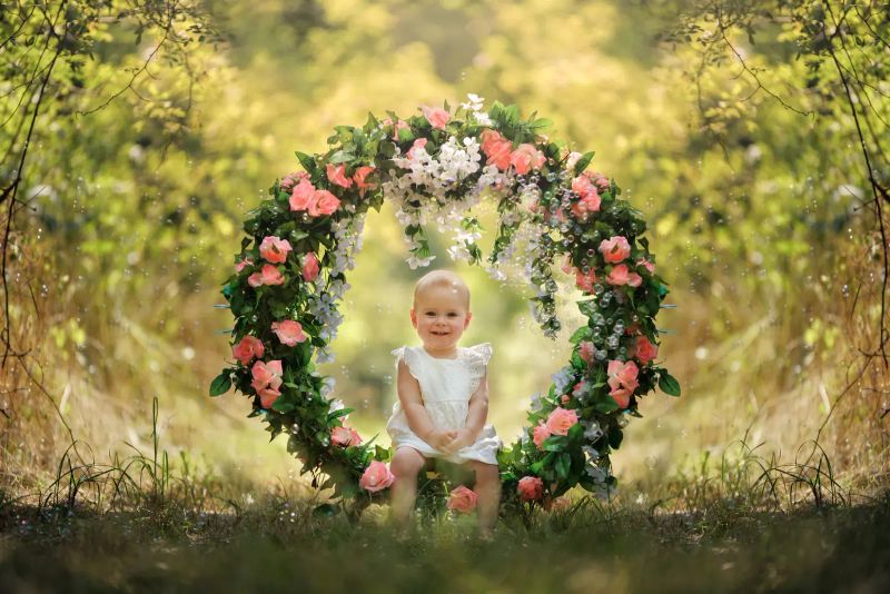 Lachendes Baby im weißen Kleid unter einem Blumenbogen — verspieltes Baby-Shooting