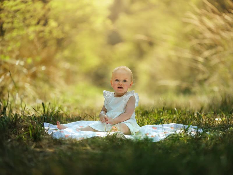 Baby im weißen Kleid sitzt fröhlich in der Sommerwiese
