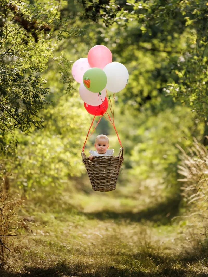Baby in einem Korb unter bunten Luftballons im Wald