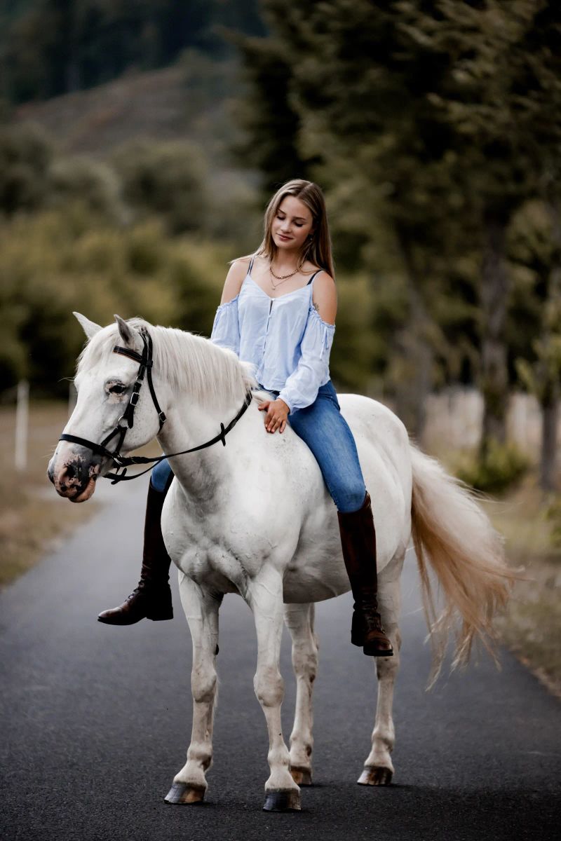 Lifestyle-Portrait einer Frau auf einem weißen Pferd im Freien