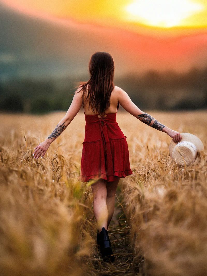 Lifestyle-Aufnahme einer Frau im roten Sommerkleid in einem Kornfeld bei Sonnenuntergang